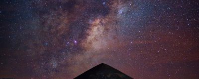 郊外草地上一位观星者躺在睡袋中仰望布满星星的银河，远处山脉轮廓清晰，氛围宁静治愈